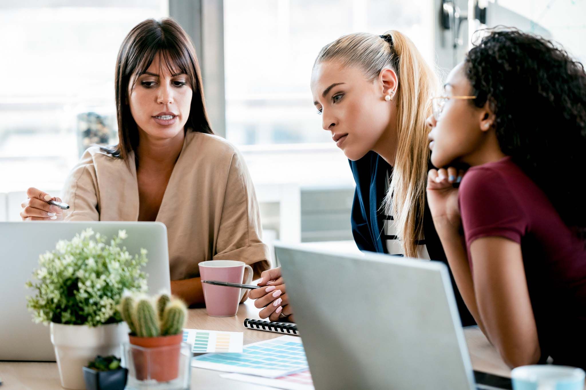 Three modern businesswomen talking and reviewing the latest work done on the computer in a joint workspace.